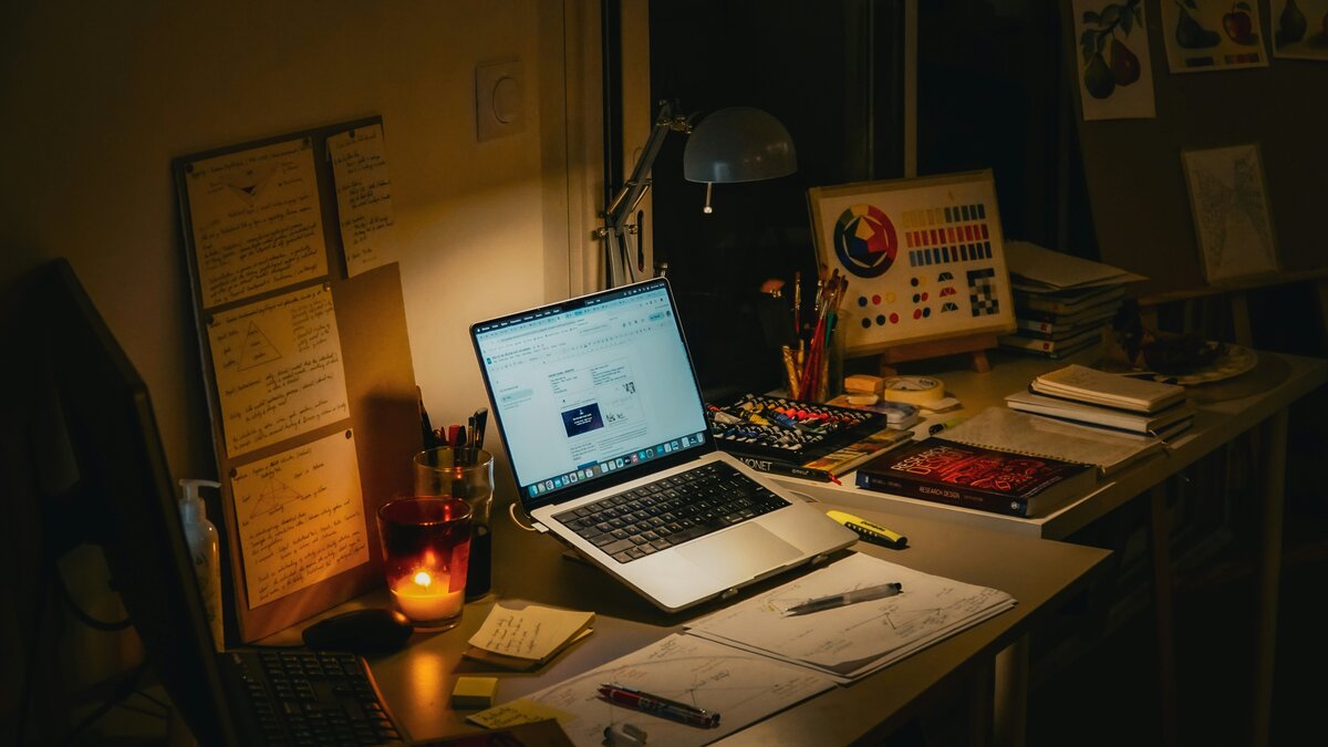 A cozy desk with a MacBook laptop surrounded by books and a candle